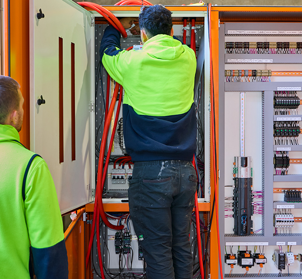Two workers in green safety vests inspect a large electrical panel as part of Progrid’s commercial electrical services