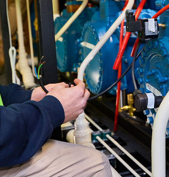A man is engaged in work on a large blue machine, providing electrical services in an industrial environment
