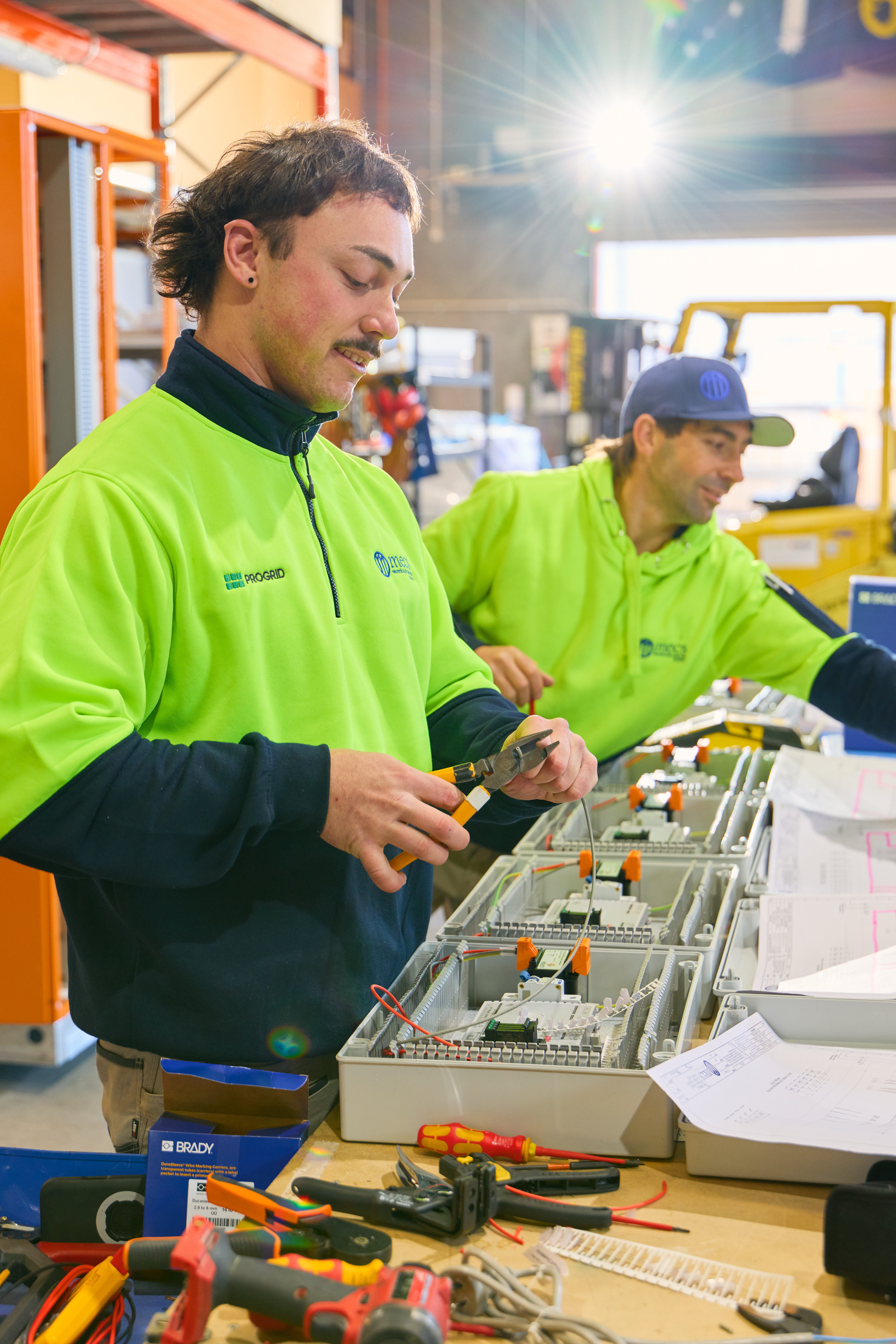 Two technicians in green vests working on a switchboard during maintenance as part of Progrid labour hire services